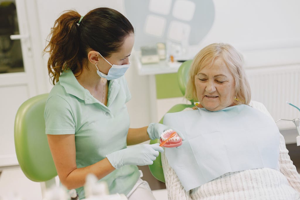 A dentist demonstrating dental health techniques to an elderly patient in a clinic.