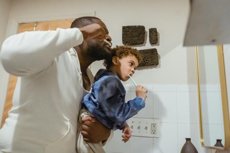 Smiling child brushing teeth with help from a parent to prevent cavities